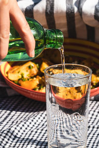 Cropped hand of woman pouring water in glass on table