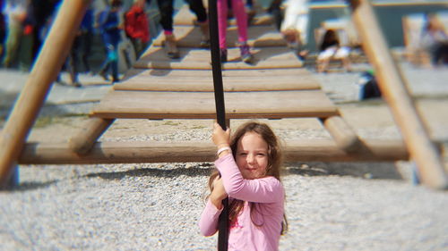 Portrait of girl hanging from rope in playground during sunny day