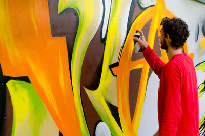 Side view of man making graffiti on wall