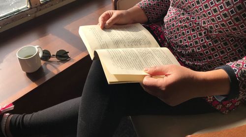 Midsection of woman reading book while sitting indoors