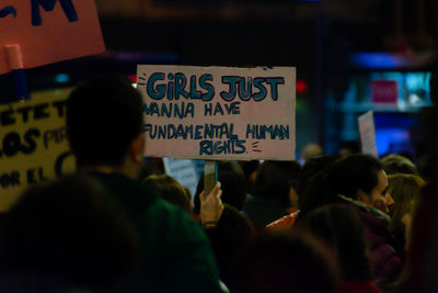 Cropped hands of person holding billboard with text by people during protest