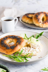 Bagel sandwich with poppy seeds with ricotta, cucumber and arugula on a plate on the table. 