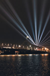 Illuminated city by river against sky at night