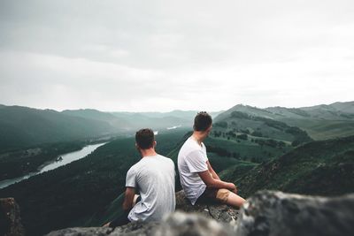Men sitting on mountain against sky