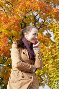 Smiling woman standing against trees in park during autumn