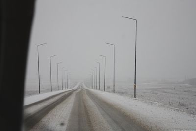 Road by snow covered landscape against sky