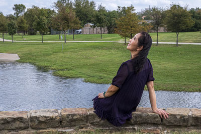 Rear view of woman sitting by pond at park