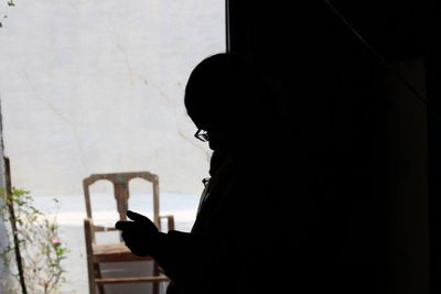 Portrait of silhouette man holding camera against window