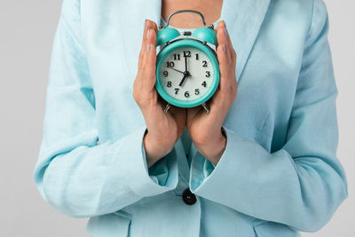 Close-up of woman holding clock over white background