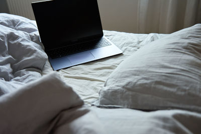 Unmade bed with pillows and crumpled bedsheets and open laptop