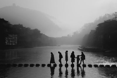 People by lake against sky during foggy weather