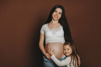 Portrait of pregnant mother with daughter against colored background