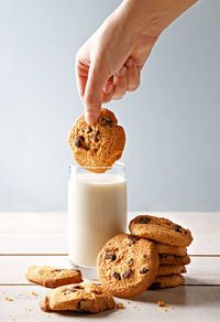 Cropped image of woman hand dipping chocolate chip cookie in milk glass on table