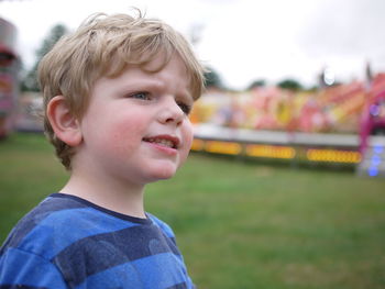 Close-up of boy looking away while standing against outdoor play equipment at playground