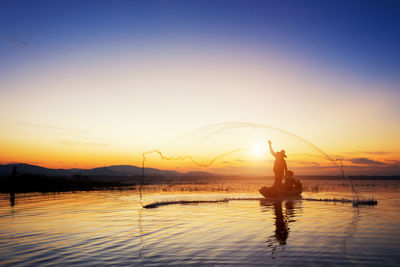 Silhouette men fishing in lake against sky during sunset
