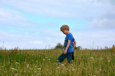 Side view of boy walking on grassy field against cloudy sky