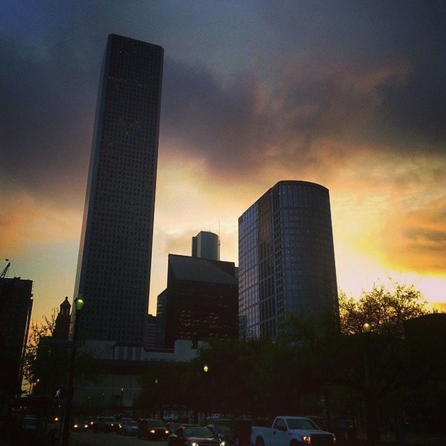 building exterior, architecture, city, sunset, skyscraper, built structure, tall - high, sky, office building, modern, tower, cloud - sky, urban skyline, cityscape, car, transportation, orange color, city life, land vehicle, silhouette