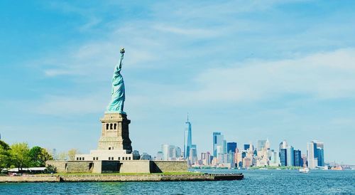 Statue of liberty and modern buildings against blue sky during sunny day