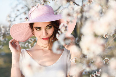 Young woman wearing hat by almond flower blossom