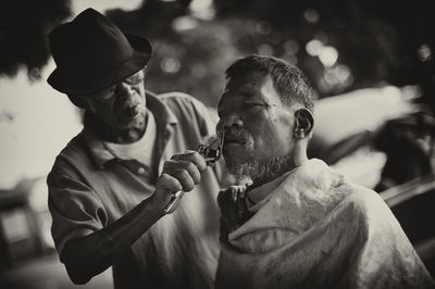 Barber trimming beard of senior man 