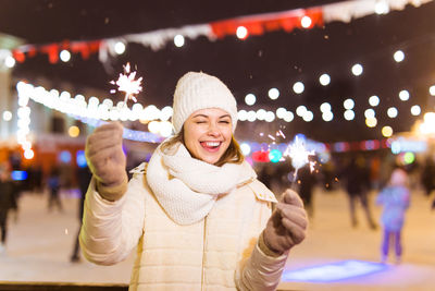 Smiling young woman standing in illuminated park at night during winter