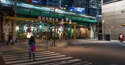 People walking on illuminated road by buildings at night