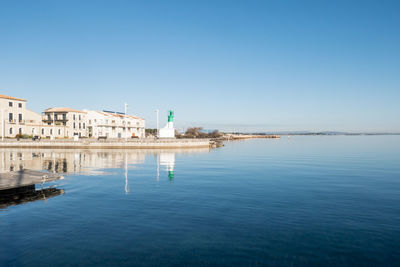Buildings in sea against clear blue sky