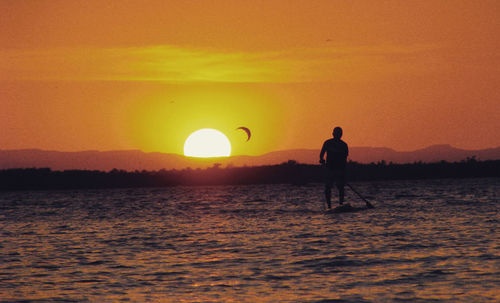 Silhouette man standing in sea against orange sky