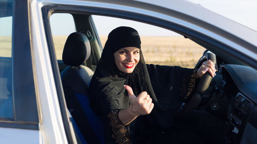 Portrait of woman wearing hijab showing thumbs up in car