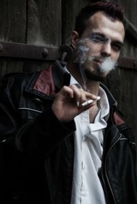 Young man smoking while standing against door