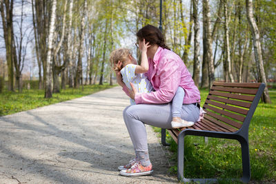 A mother cradles her daughter up and down while sitting on a bench in a city park.