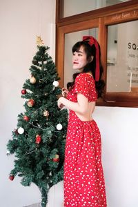 Young woman in red dress standing against christmas tree