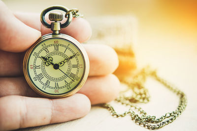 Close-up of hand holding pocket watch on table