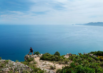 Rear view of man standing on cliff by sea against sky