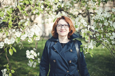 Confedent middle aged armenian woman in a blue trench coat under the blooming tree. spring season 