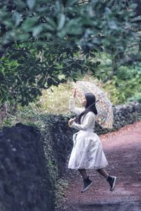 Full length of woman in mid-air holding umbrella 