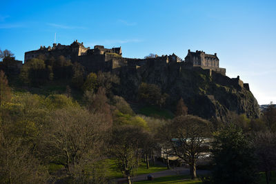 Low angle view of edinburgh castle on mountain against blue sky