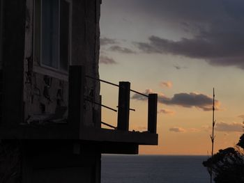 Silhouette built structure by sea against sky at sunset