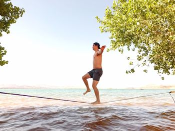 Side view of shirtless man tightrope walking over sea