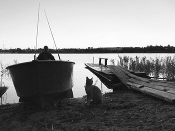 Rear view of men fishing in lake against clear sky