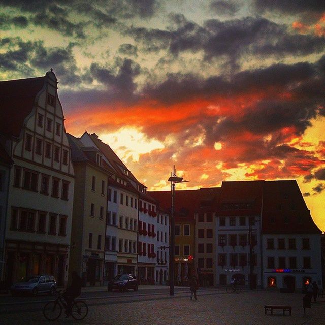 building exterior, architecture, built structure, sunset, transportation, land vehicle, car, sky, mode of transport, cloud - sky, street, city, orange color, cloudy, road, residential building, building, residential structure, cloud, city life