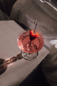 Pink sparkling wine drink with strawberry heart garnish next to bed in the sunlight