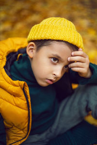 Portrait of a fashionable child boy autumn sitting on a trail in orange leaves in the afternoon