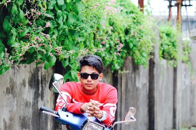 Young man wearing sunglasses while sitting on scooter by plants