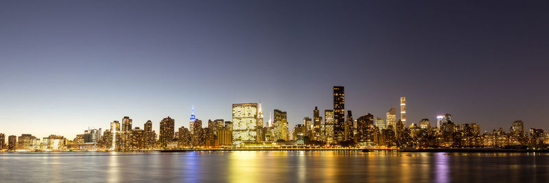 Illuminated buildings by river against sky in city