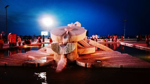 People in illuminated park against sky at night