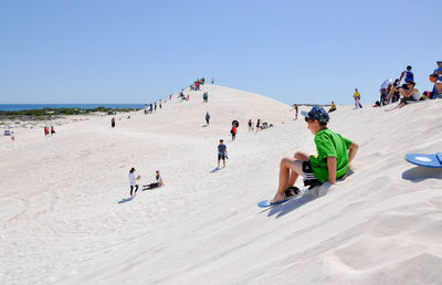 People at beach against clear blue sky