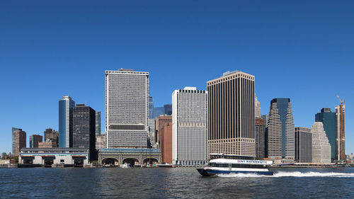 Sea by modern buildings against clear blue sky