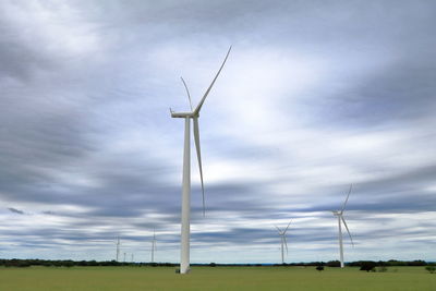 Low angle view of wind turbines on field against sky