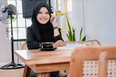 Portrait of young woman sitting on table at home